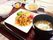 白いご飯や野菜と肉の炒め物、みそ汁、フルーツ、野菜の小鉢などが並んだトレー。
