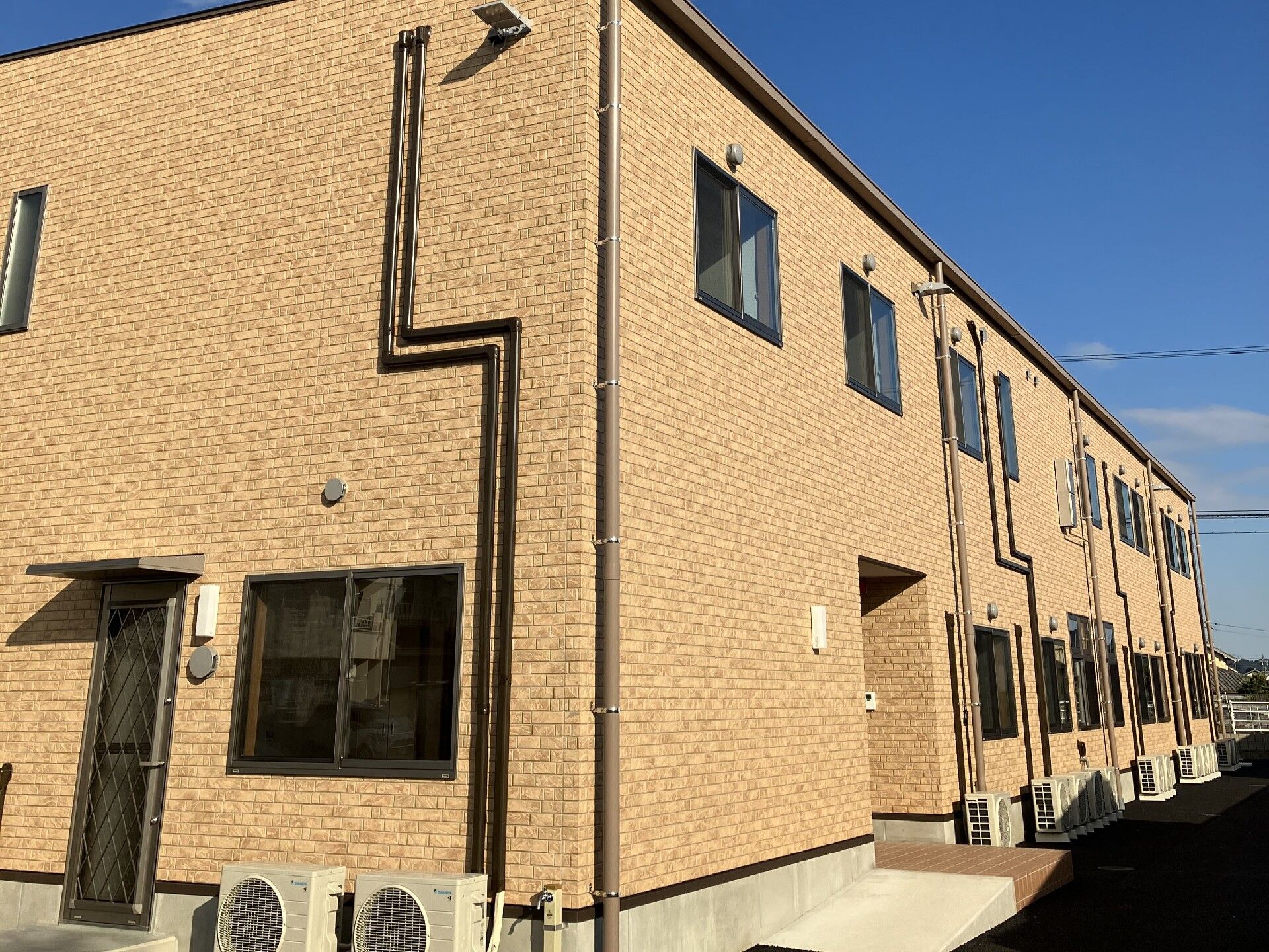 広い駐車場が付いた２階建ての建物は日当たりがよく、エル字型。玄関先には屋根があり、階段とスロープが付いている。