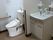 オレンジの呼び出しボタンや手すりが設置されたトイレと収納や鏡が設置された洗面所が並んで設置されている。