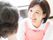 ピンクのエプロンを付けた女性スタッフが笑顔で高齢女性の話を聞いている。