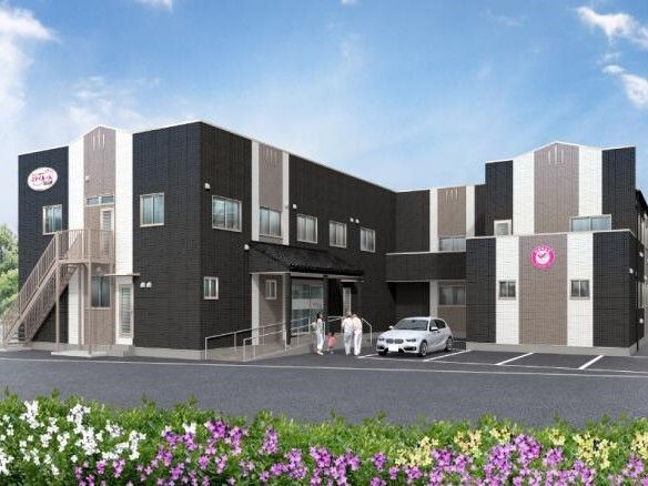 ２階建ての建物はエル字型でダークグレーの外壁。玄関先には手すり付きのスロープが付いている。