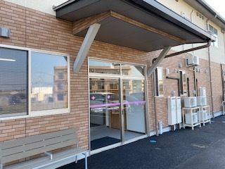 カーディガンを着た高齢女性が車いすに座り、そばにいるポロシャツを着た若い女性スタッフと手を重ね合っている。