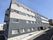 4階建ての建物の外壁はダークグレーでホーム名が書かれている。玄関先には草木が植えられている。