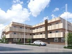 広い駐車場には車が止まっている。3階建てのエル字型の建物はベージュ系の外壁で日当たり良好。