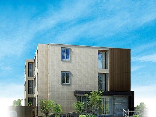 ３階建ての建物。ベージュとブラウンの外壁で玄関には緩やかなスロープと階段、屋根が付いている。