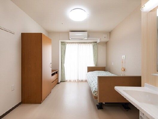 寝具付きのベッドや収納家具、エアコンなどが付いた部屋。ベッドサイドには緊急通報装置もある。
