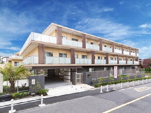 道路に面して建っている3階建ての建物は日当たりのいい場所にあり、建物の周りには草木が植えられている。