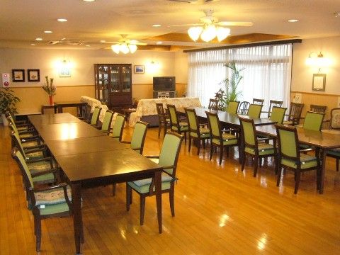 窓から入る自然光と、大きな照明から光が落ちる広々とした食堂。ダイニングセットのほか、テレビ前にソファがある。