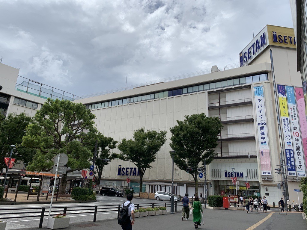 近くには駅があり交通の便が良い立地になっている。周りには飲食店やバス停などがあって、旗や掲示板が立っている。