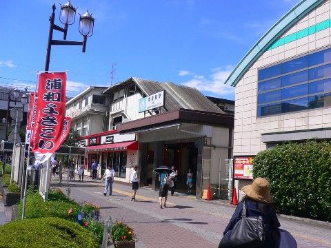 近くには駅があり交通の便が良い立地になっている。周りには飲食店やバス停などがあって、旗や掲示板が立っている。