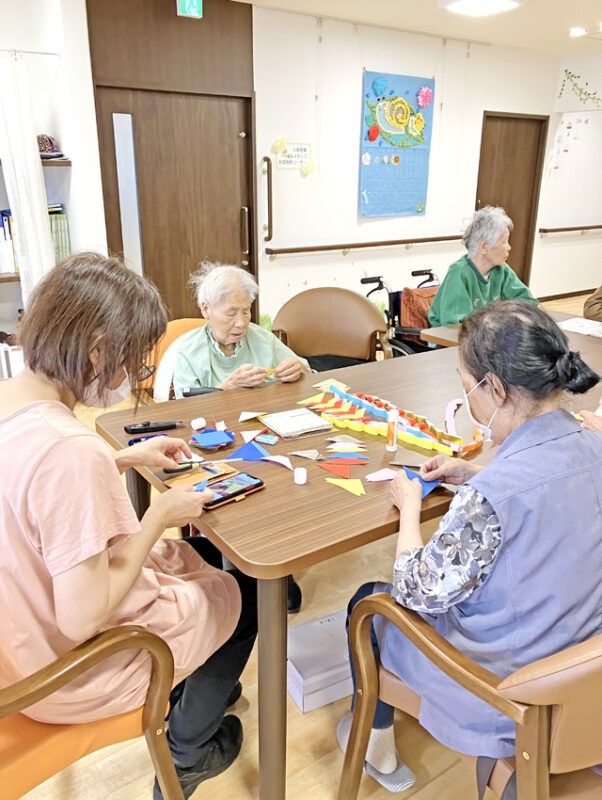 背の高いポロシャツを着た若い女性スタッフは両サイドに立っている高齢女性たちと手をつないでいる。