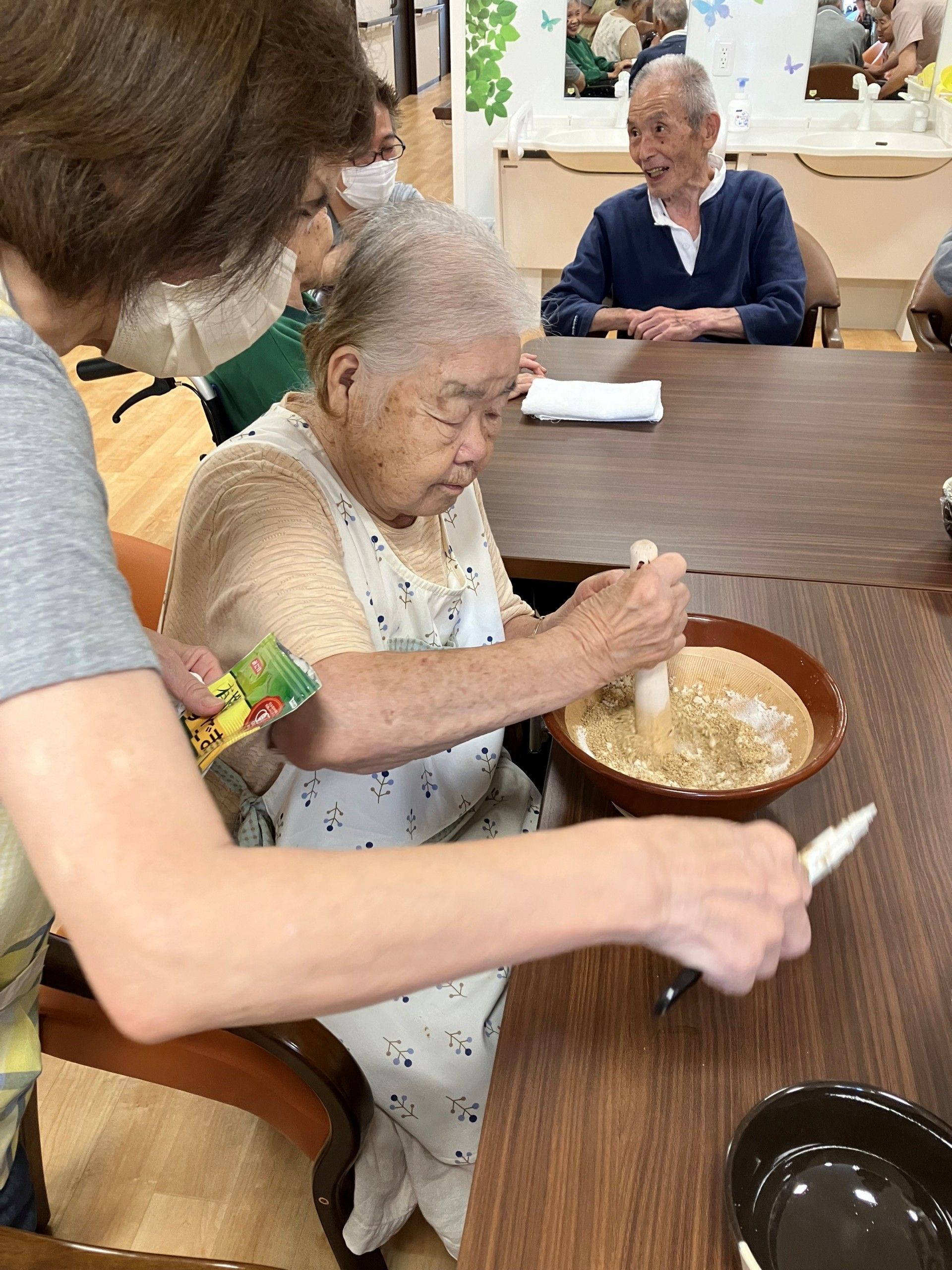 テーブルに椀を並べている高齢女性とその椀に汁物を注いでいる高齢女性。