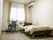 レースカーテンとカーテンが付いた大きな窓が付いているフローリングの部屋には寝具付きのベッドが置かれ、車いすもある。