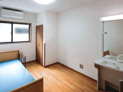 クローゼットやエアコン、洗面所、介護ベッドが設置されたフローリングの部屋にはカーテンのない窓がある。