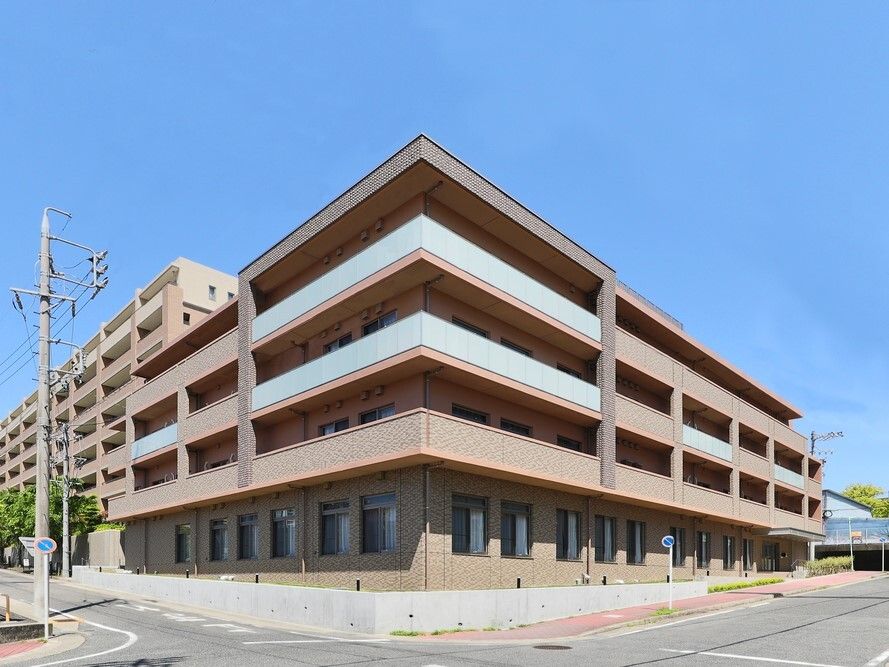 角フロアにベランダが付いたブラウン系の外壁の４階建ての建物は日当たりのいい場所に建っている。