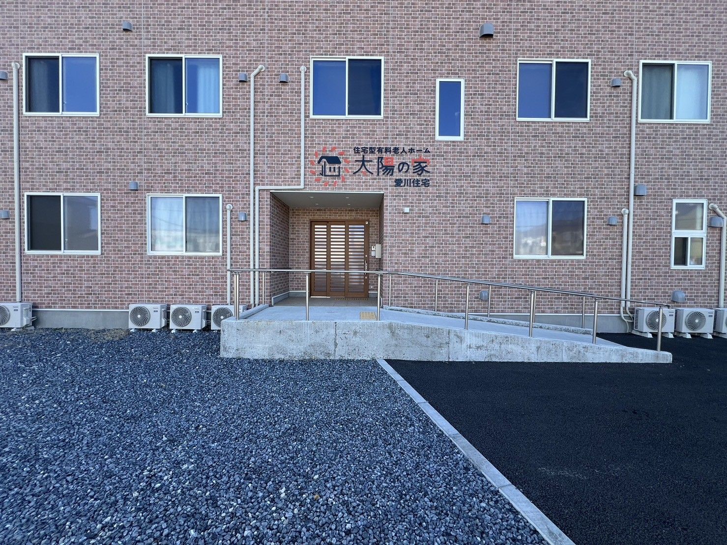 高齢男性の立ちあがろうとしているところを笑顔で介護に当たっているボーダー柄のエプロンを付けた女性スタッフ。