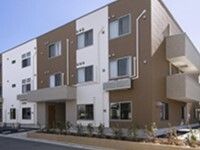 ブラウンと白の3階建ての建物は玄関には屋根があり、角フロアにベランダが付いている。