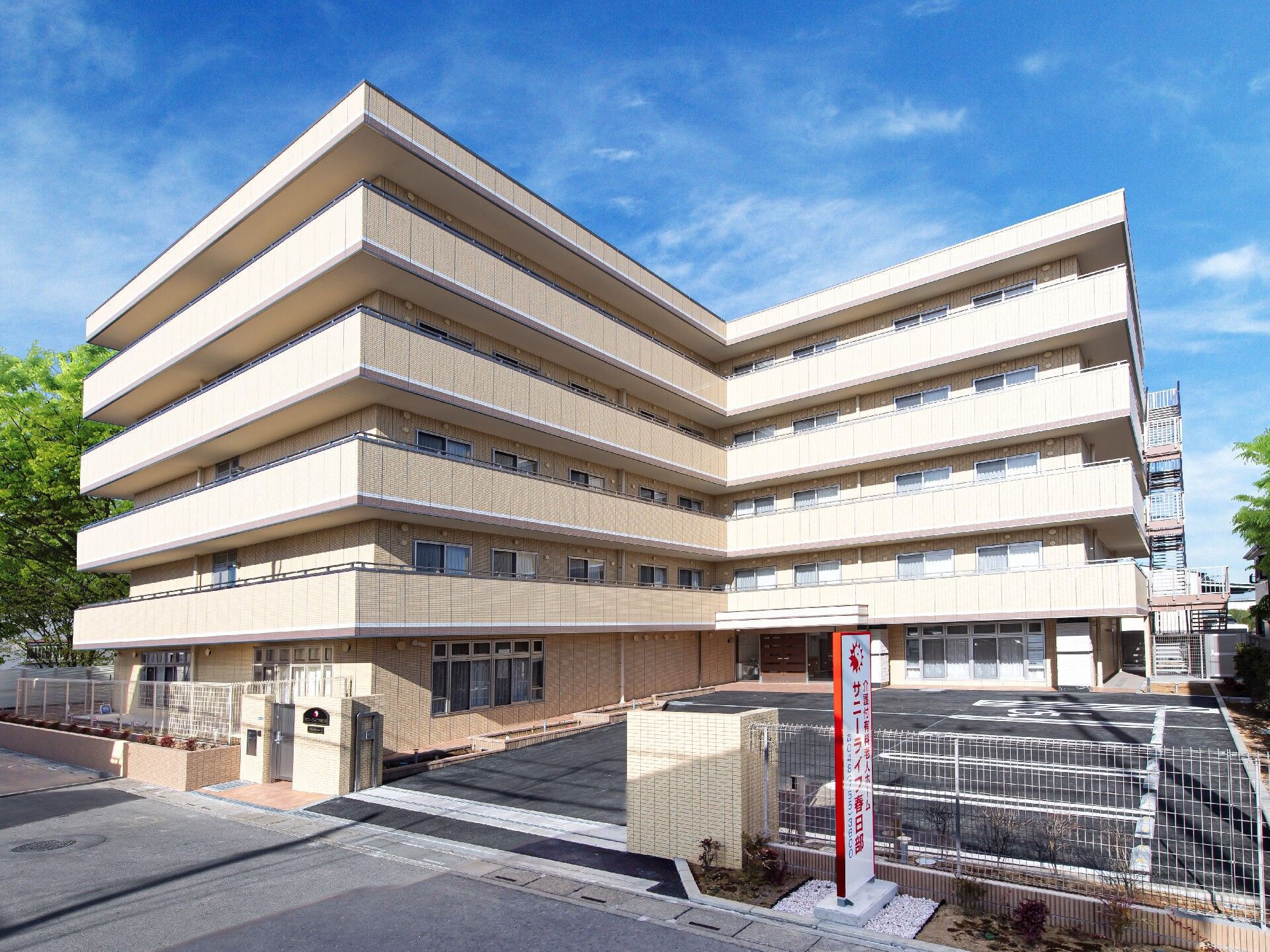 エル字型のベージュの外壁の5階建ての建物は日当たり良好で門の周りには草木も植えられている。