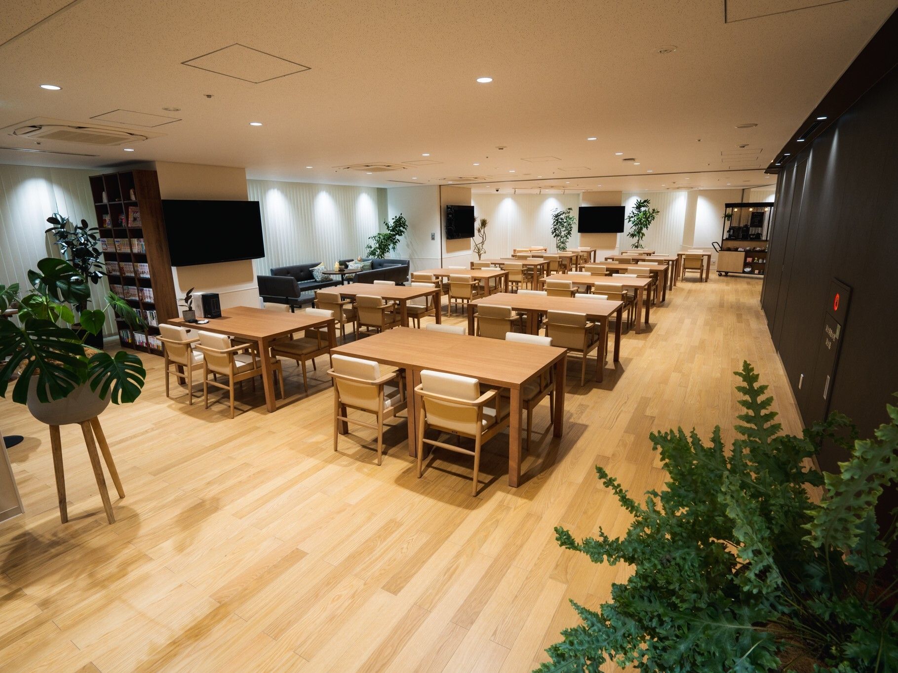 木製のダイニングテーブルセットがたくさん置かれている食堂には多くの観葉植物が飾られている。