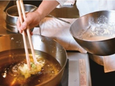白い調理用の服を着たスタッフが大きな油鍋の中で天ぷらを揚げている様子。
