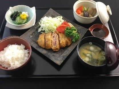 たっぷりの野菜が使われたトンカツ定食。トンカツはミルフィーユ状になっていて味噌汁や白いご飯、野菜のおかずが添えられている。