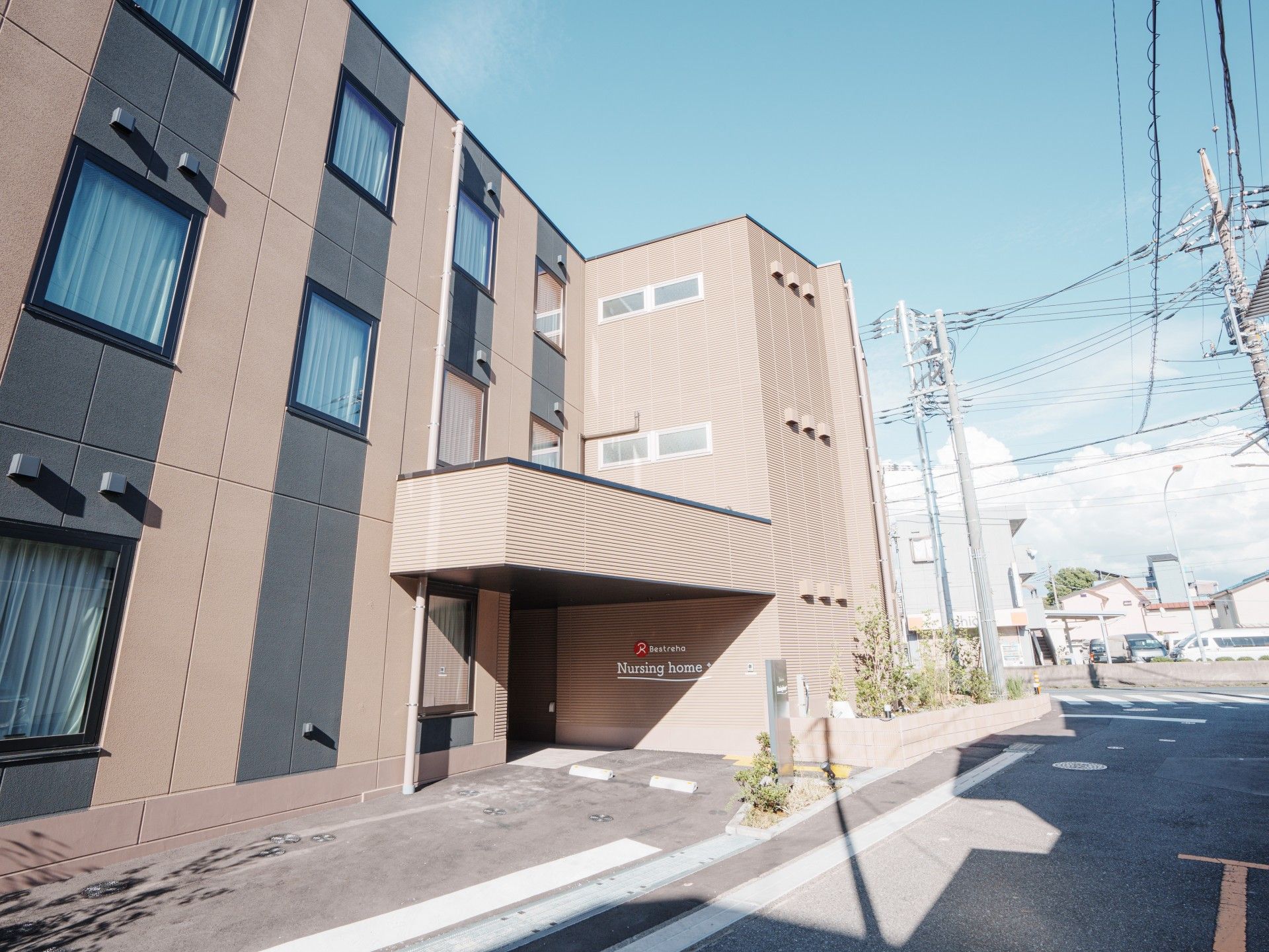 ブラウン系の外観の3階建ての建物の周りには草木も植えられ、玄関先には屋根が付いている。