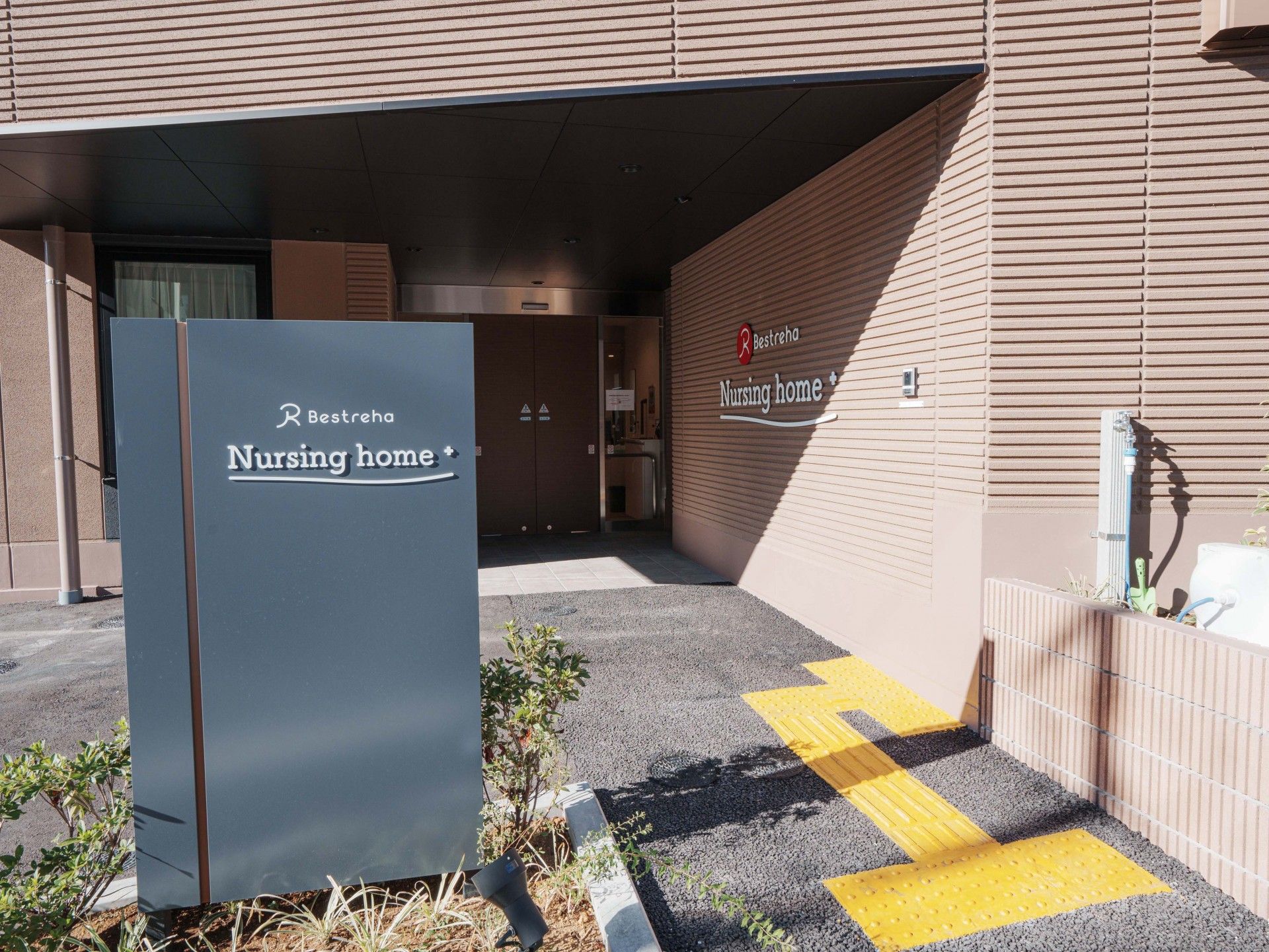 ホーム名が玄関の横の外壁に書かれ、館銘板も建っている。玄関先には大きな屋根も付いている。