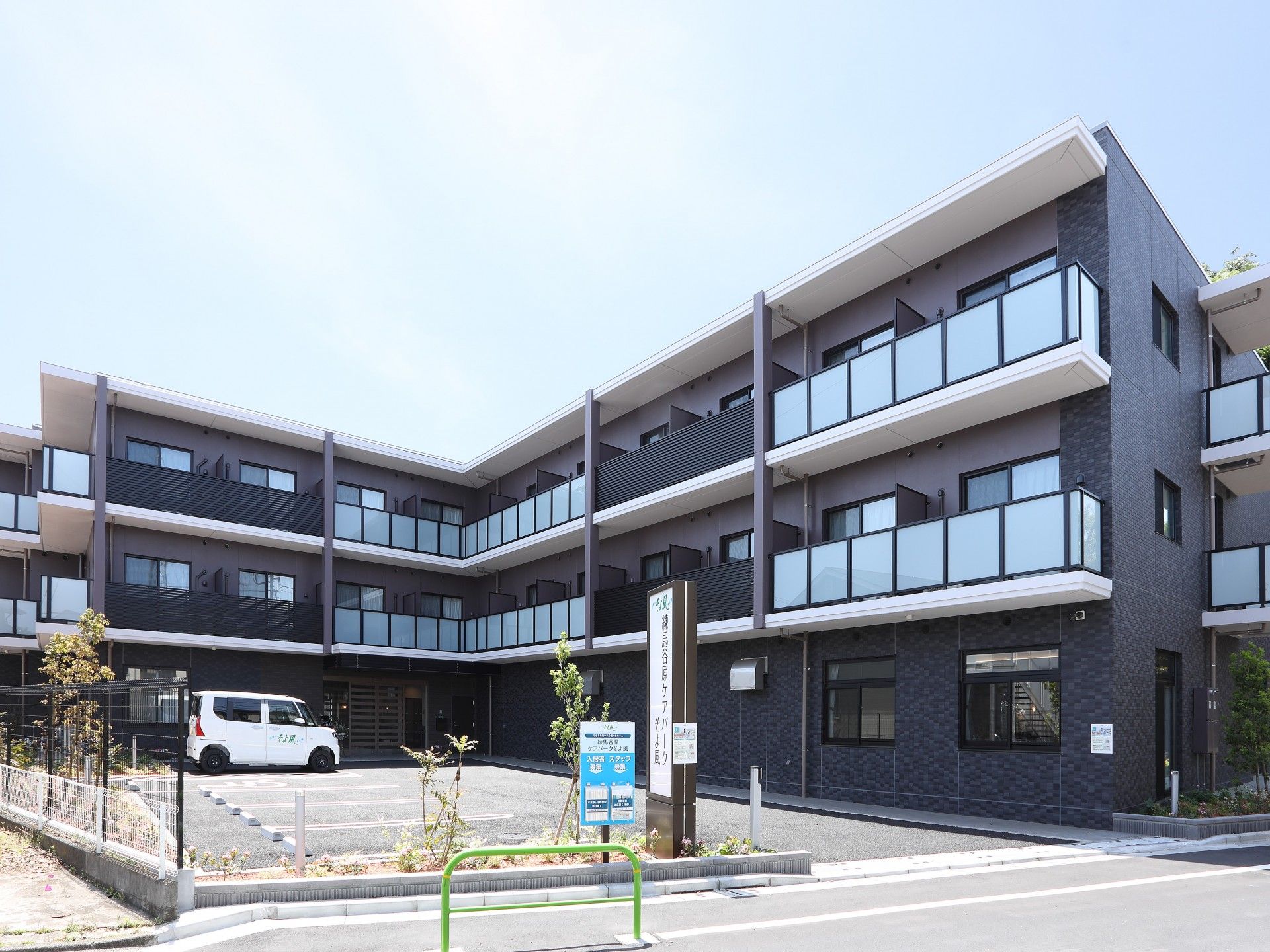 エル字型の3階建ての建物は日当たりのいい場所に建っていて、敷地内には駐車場があり、車が止まっている。