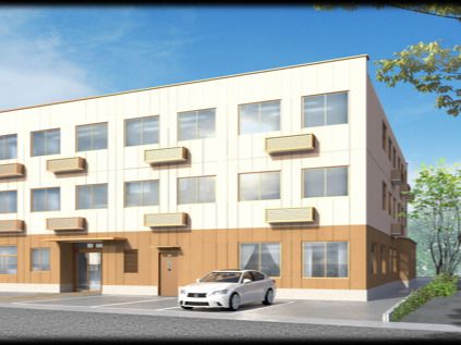 白とブラウンの外壁の3階建ての建物は日当たりのいい場所に建っていて、目の前には駐車場がある。