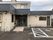 ベージュの外壁の２階建ての建物の玄関先には手すり付きのスロープがあり、屋根も付いている。