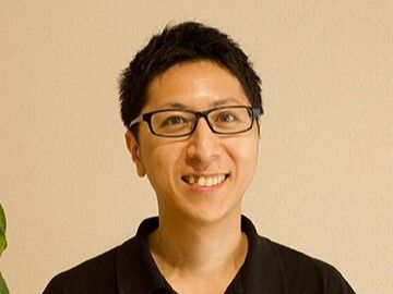 黒ぶちの眼鏡をかけた男性スタッフは短髪で黒髪。八重歯が目立つ笑顔が印象的。