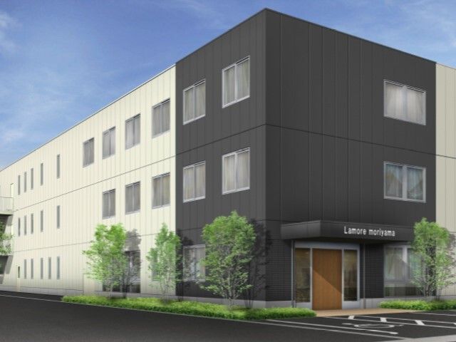 白とダークグレーの外観の3階建ての建物は日当たりのいい場所に建っていて、玄関先にはホーム名が書かれた屋根がある。