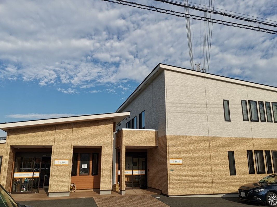 ベージュと白の外壁の2階建ての建物の前には駐車場も完備されている。日当たりのいい場所に建っている。