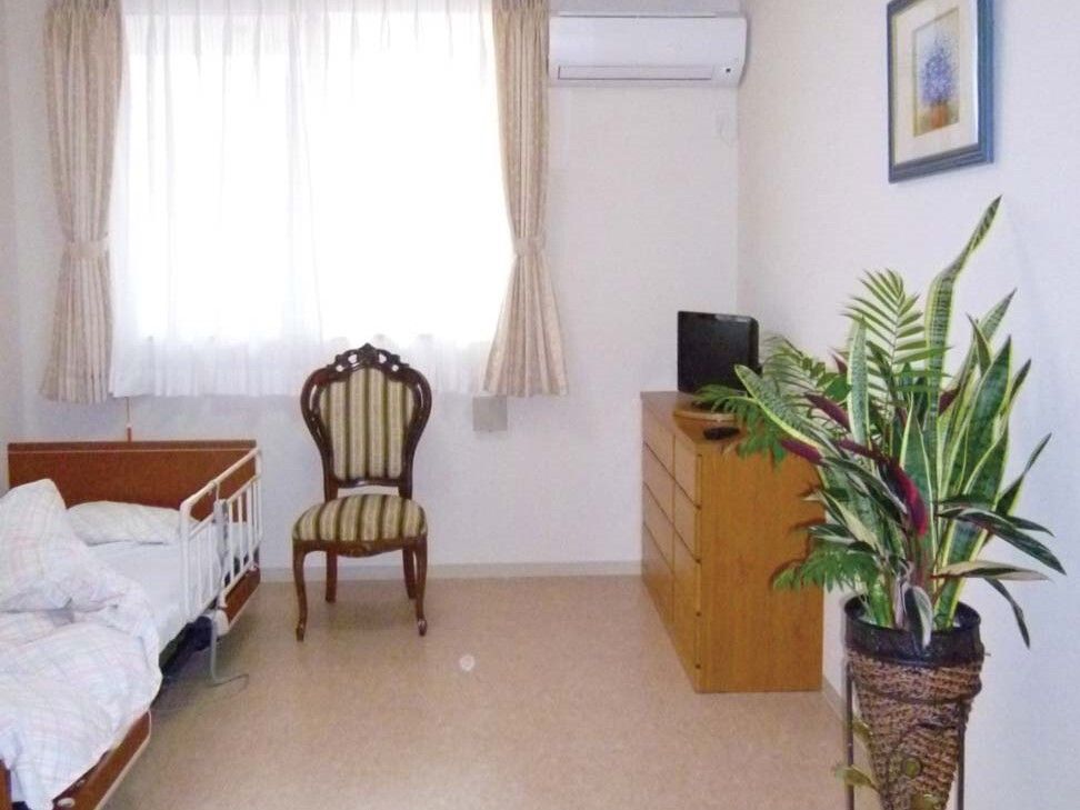 エアコンや寝具付きのベッドがある部屋には大きな窓があり、観葉植物やいすが置かれている。