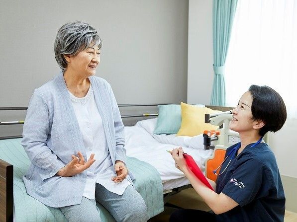 エプロンを付けた若い女性スタッフとカーディガンを着た高齢女性がカルテのようなものを見ながら話している。