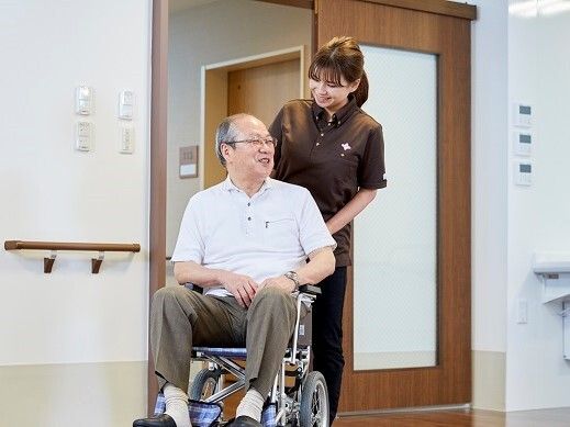 笑顔で鏡を見ているポロシャツを着た若い女性スタッフと白髪の高齢女性。女性は座っている。