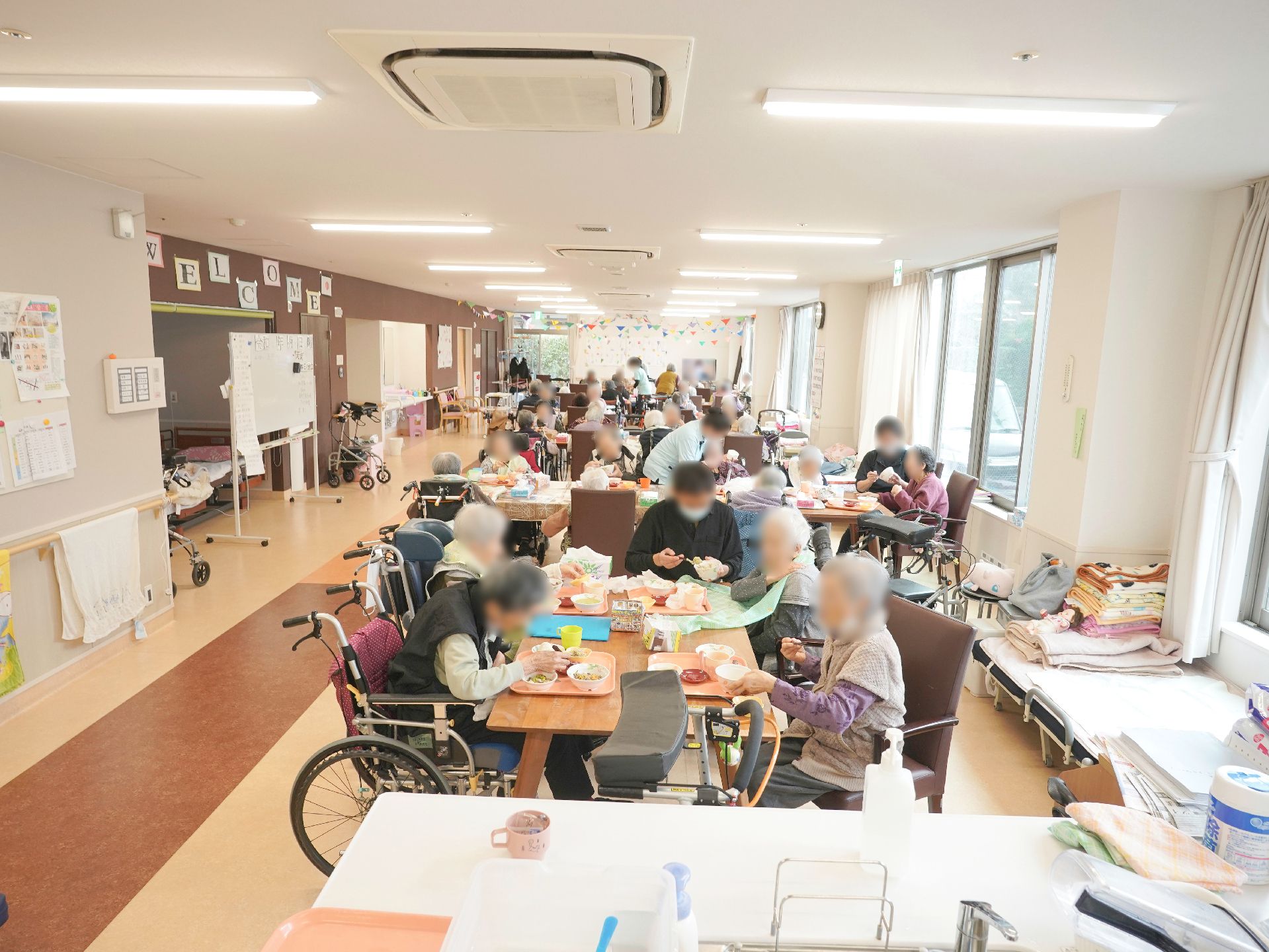 屋外で笑顔で過ごしている車いすの高齢女性と付き添いのエプロンを付けた女性スタッフ。