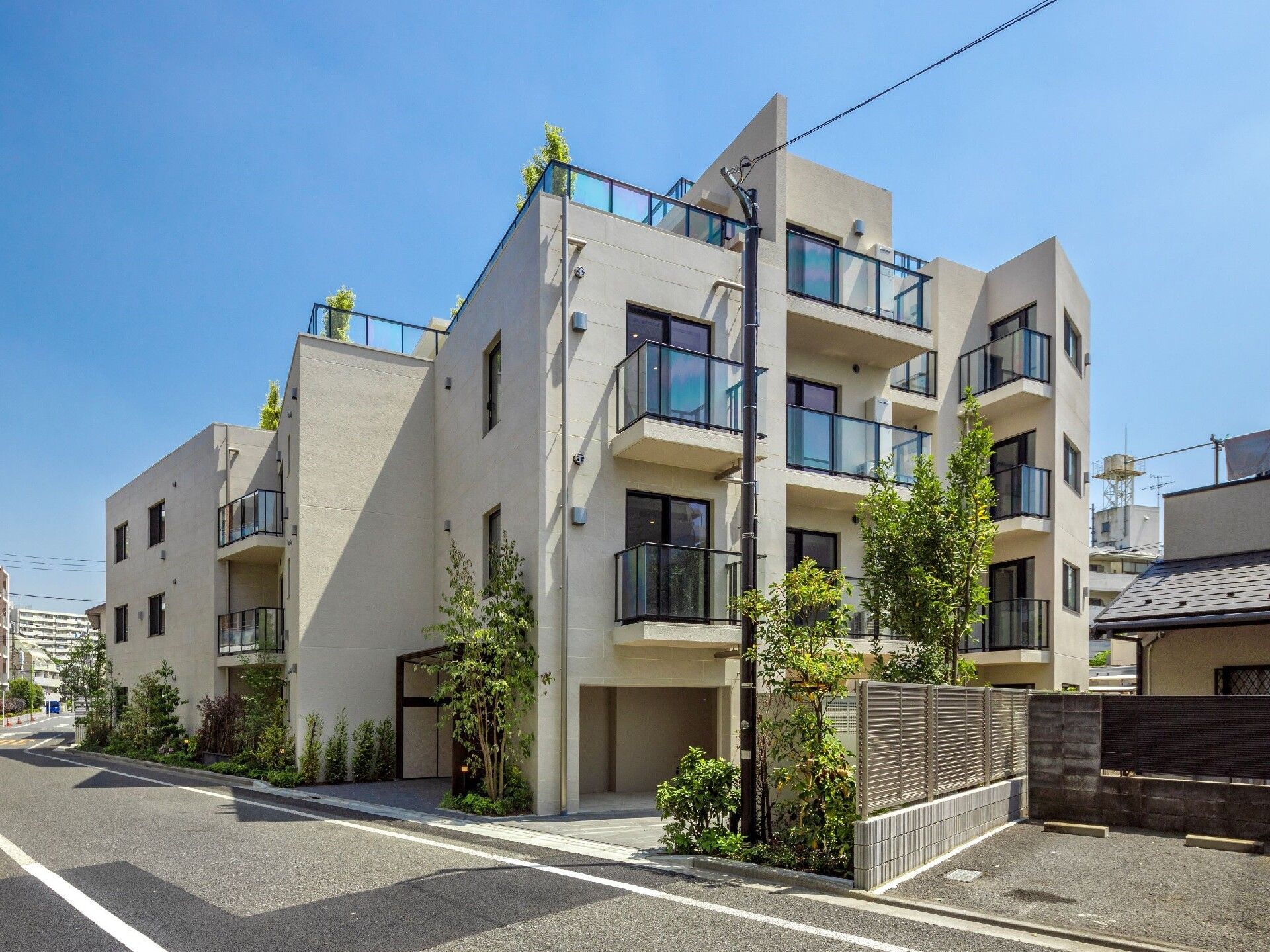 ベージュの外壁の3階建ての建物の周りと屋上には草木が植えられている。駐車場もある。
