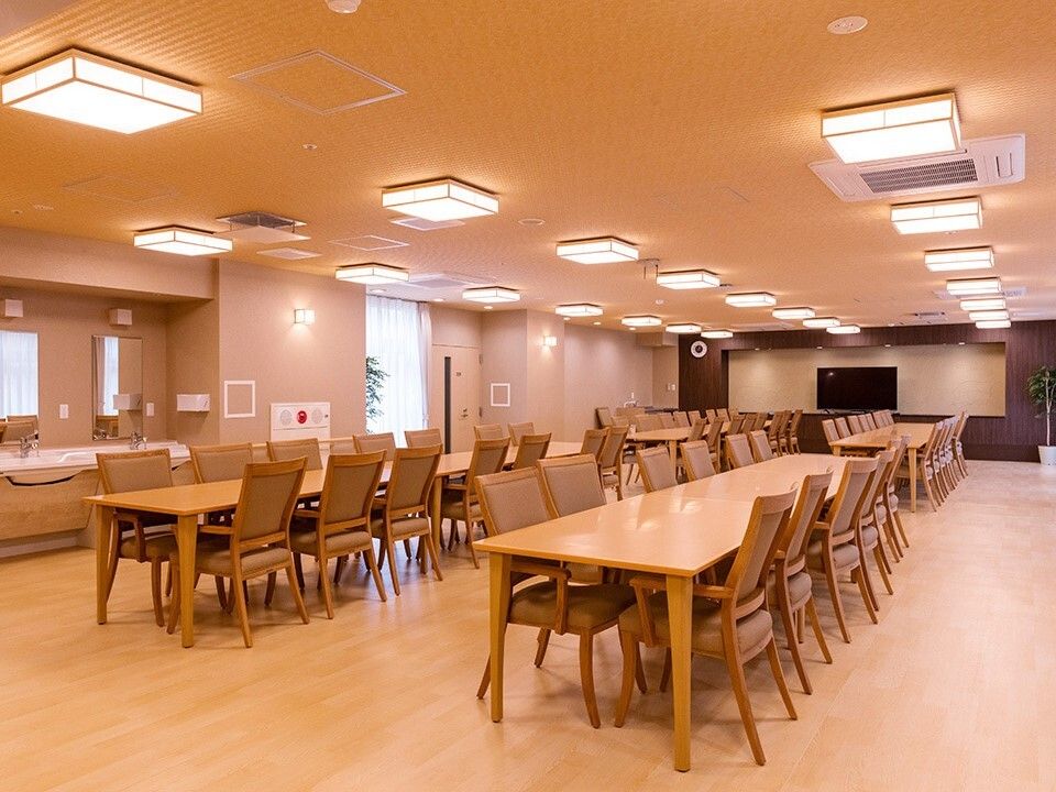 木製のダイニングテーブルが複数置かれている食堂には観葉植物が置かれ、テレビも設置されている。