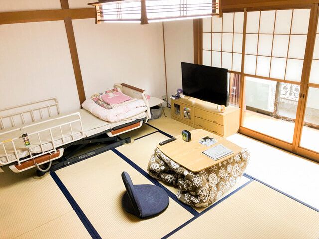畳敷きの和室にはテレビや介護ベッド、こたつ、座椅子などが置かれ、和風の照明が付いている。