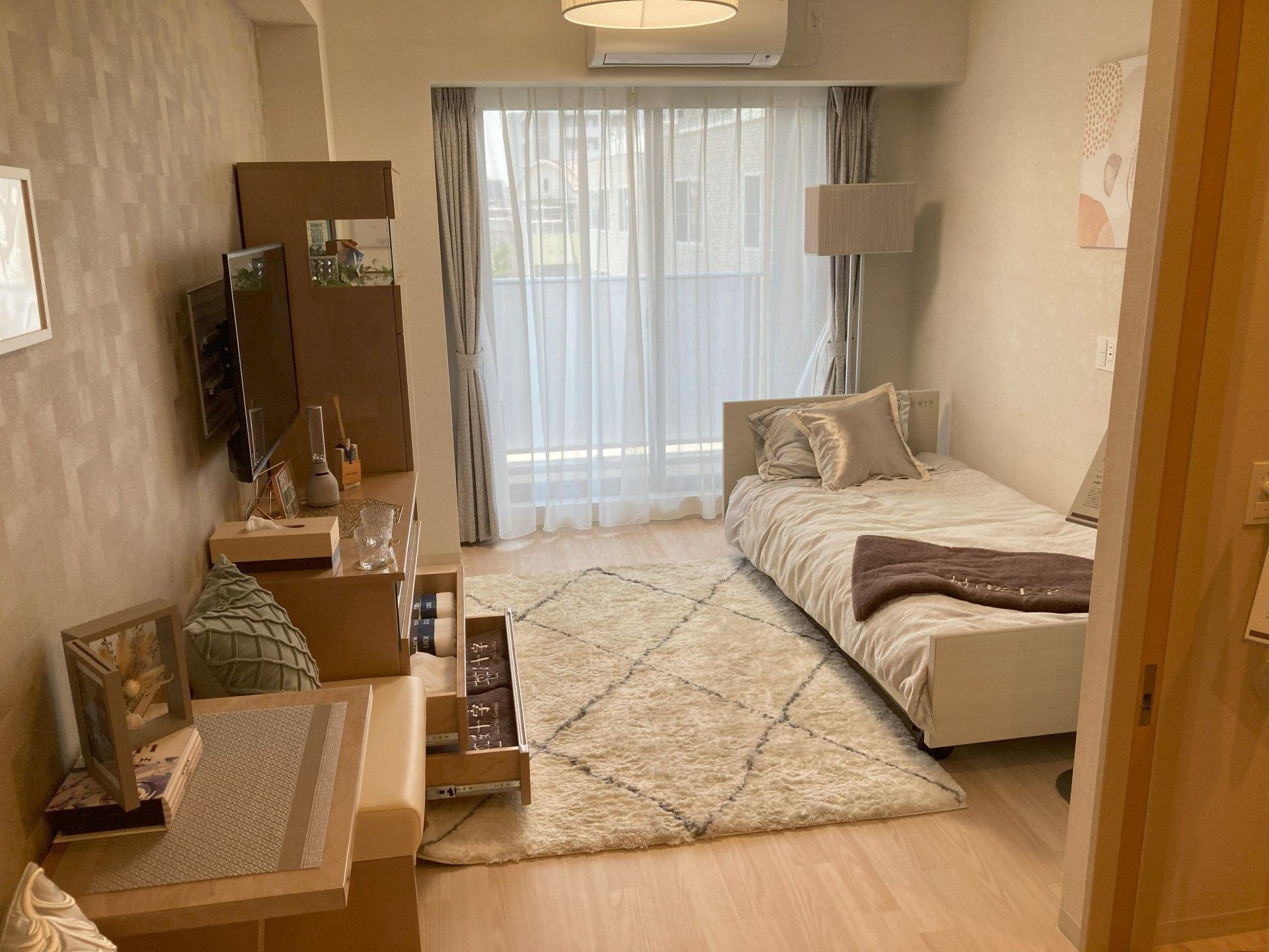 フローリングの部屋には家具や家電があり、レースカーテンとカーテンが付いたおおきな窓もある。