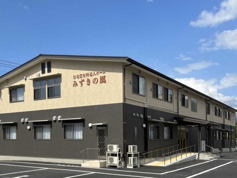 日当たりのいい場所に建っている２階建ての建物の外壁はベージュとブラウンでホーム名が外壁に書かれている。