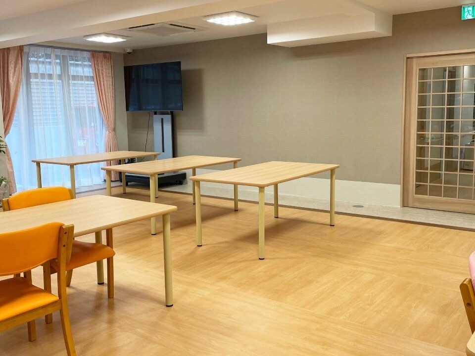 木製のダイニングテーブルが複数置かれた食堂には大きなテレビもあり、テーブルにはまばらに椅子がセットされている。