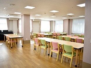 ライトグリーンやピンクの椅子がセットされている木製のダイニングテーブルセットが複数置かれた食堂。