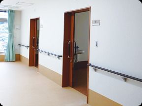 手すりが付いた廊下には居室のスライド式のドアが設置されていて、突き当りにはカーテンが付いたおおきな窓がある。