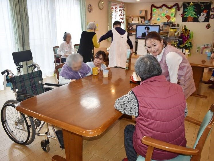 車いすもセットされたダイニングテーブルを囲んで話している高齢女性たちとスタッフたち。マンツーマンで話している。