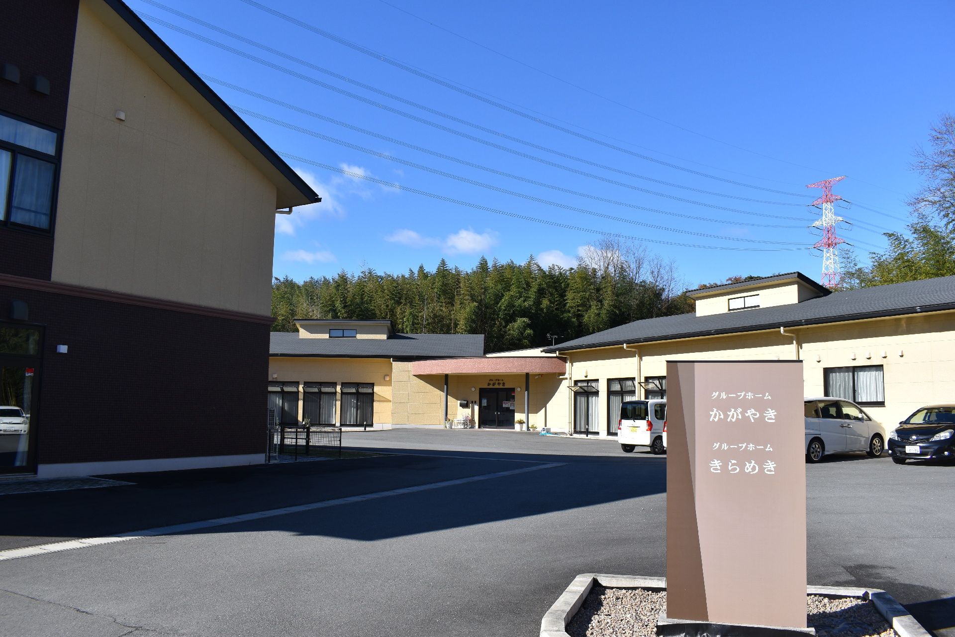 青空の下に建っている２棟の施設。いずれもグレーの屋根が付いた平屋建ての建物で手前には館銘板がある。