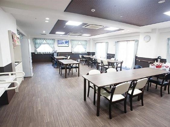 木製のダイニングテーブルセットが複数置かれている食堂にはレースカーテンとカーテンが付いたおおきな窓がある。