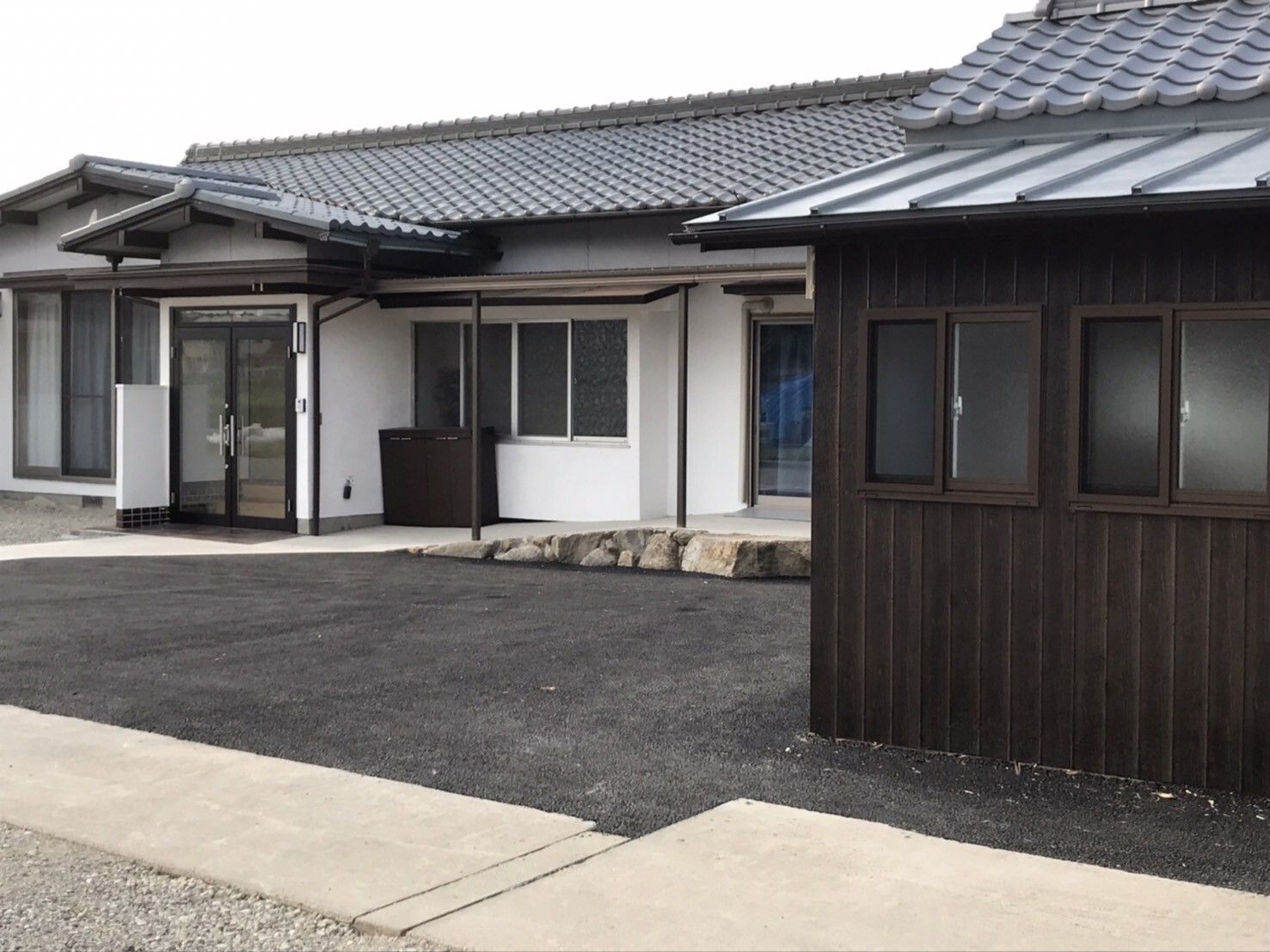 グレーの瓦屋根が付いた平屋建ての建物は白壁で、すっきりとしたデザイン。敷地内には駐車場もある。