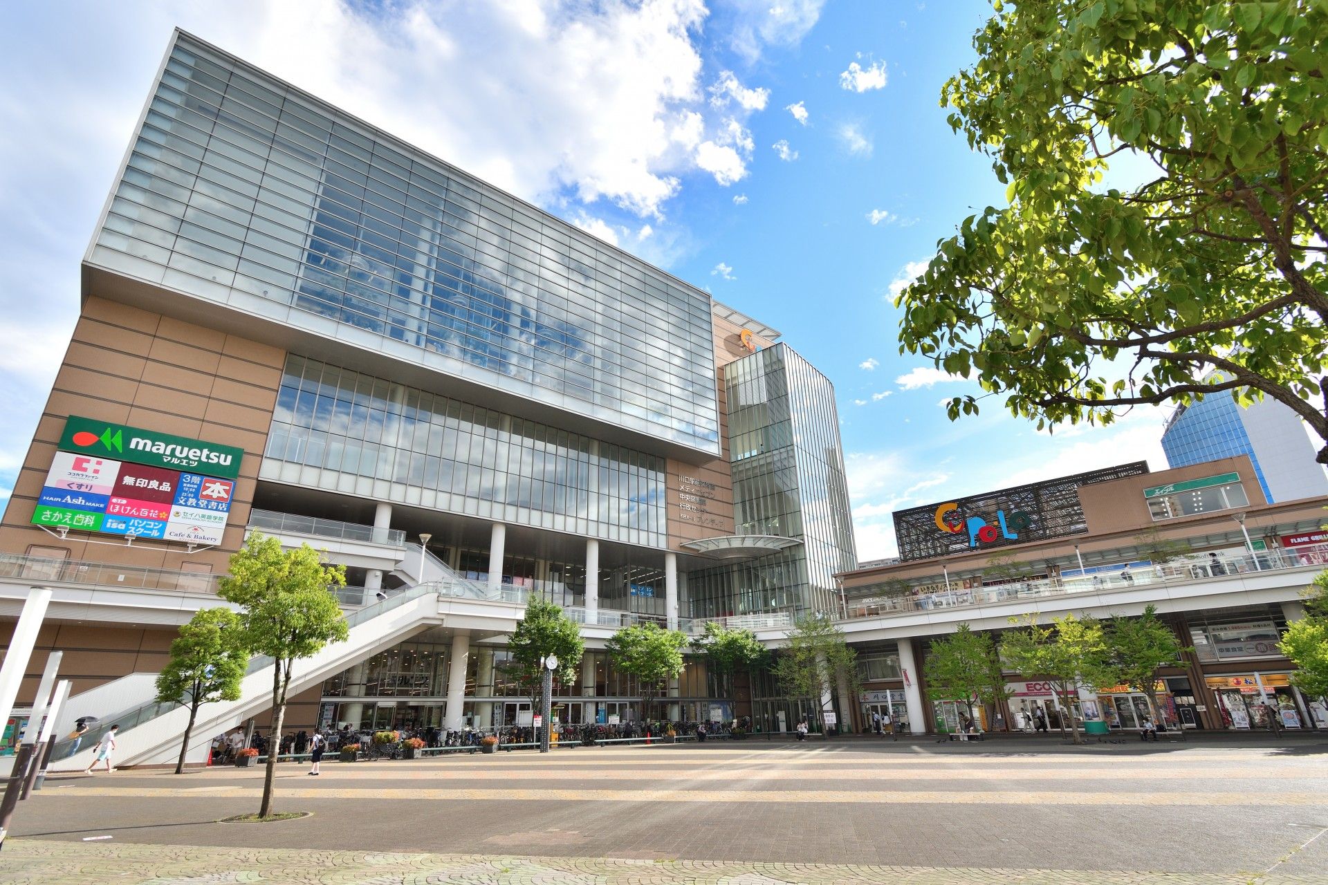 斜め屋根の佇まいが印象的な高層ビルが建っている。手前の広場では、子どもたちが楽器を演奏する姿が見られる。